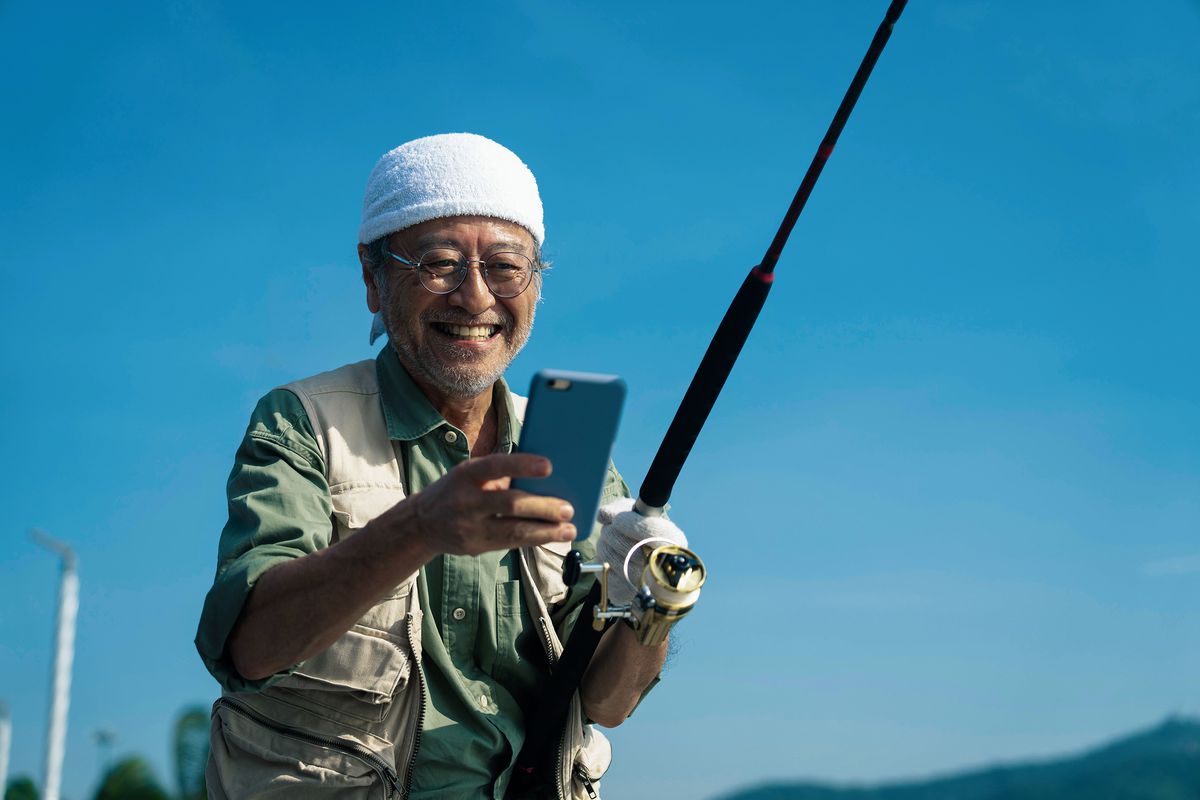 An older fisherman smiling at his phone
