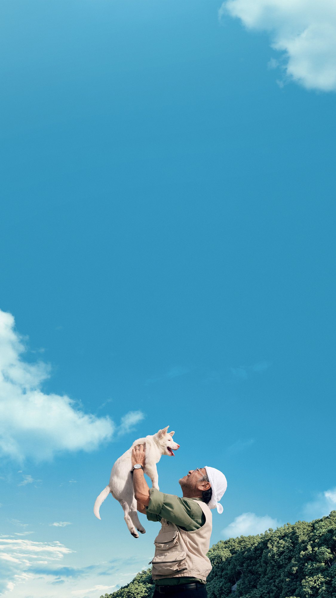 A man lifting a white puppy into a bright blue sky