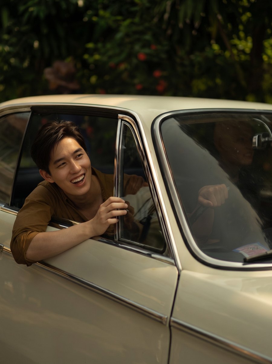 Thanapob Leeratanakachorn laughing as he leans out of a vintage car window in One for the Road