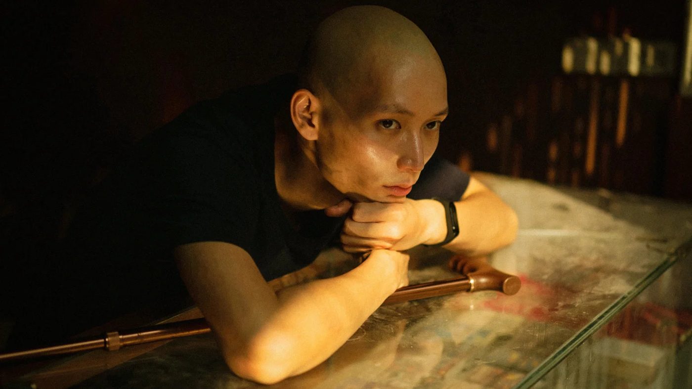 A young man with a shaved head resting on a glass counter