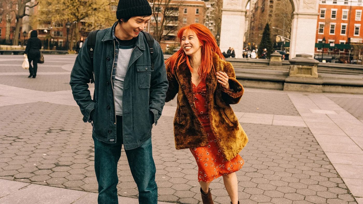 A young man and a red-haired woman laughing in a city square