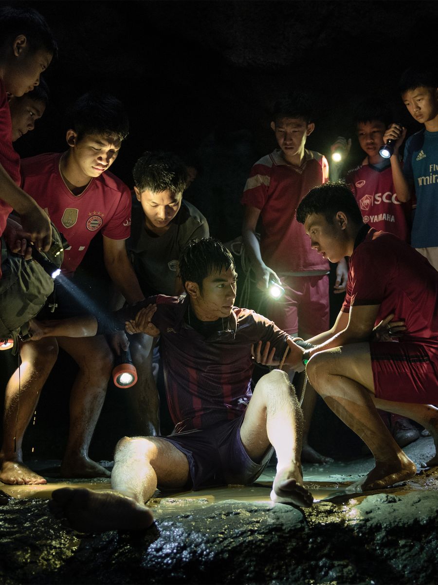 Coach Eak sits in shallow water in the cave as the boys gather around him with torches, a scene from Thai Cave Rescue