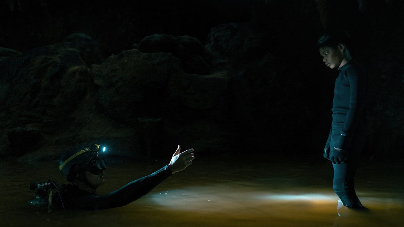 A diver in a cave pool reaching out to a boy